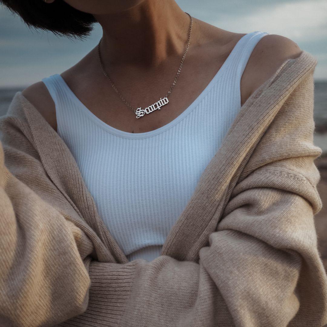 woman in white tank and tan sweater wearing gold name necklace